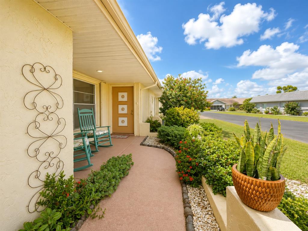 A tan house exterior features a covered walkway, a brown front door, and rocking chairs — 310 FAIRCROSS CIRCLE, SUN CITY CENTER, FL