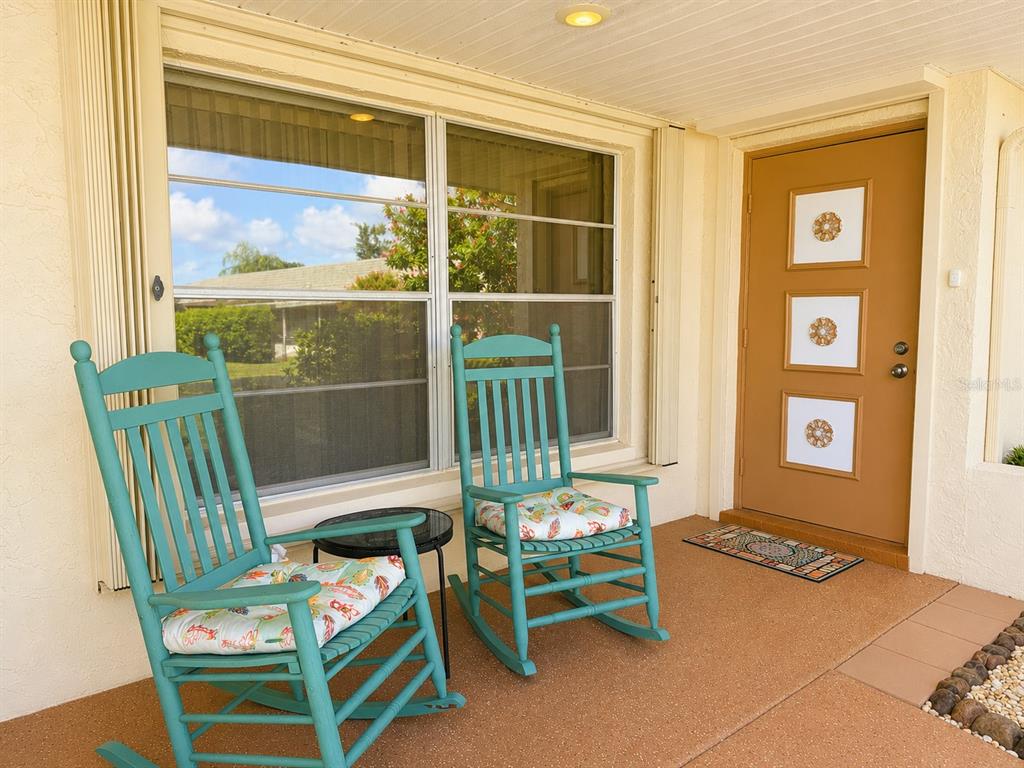 A covered porch features two teal rocking chairs with patterned cushions and a brown door — 310 FAIRCROSS CIRCLE, SUN CITY CENTER, FL