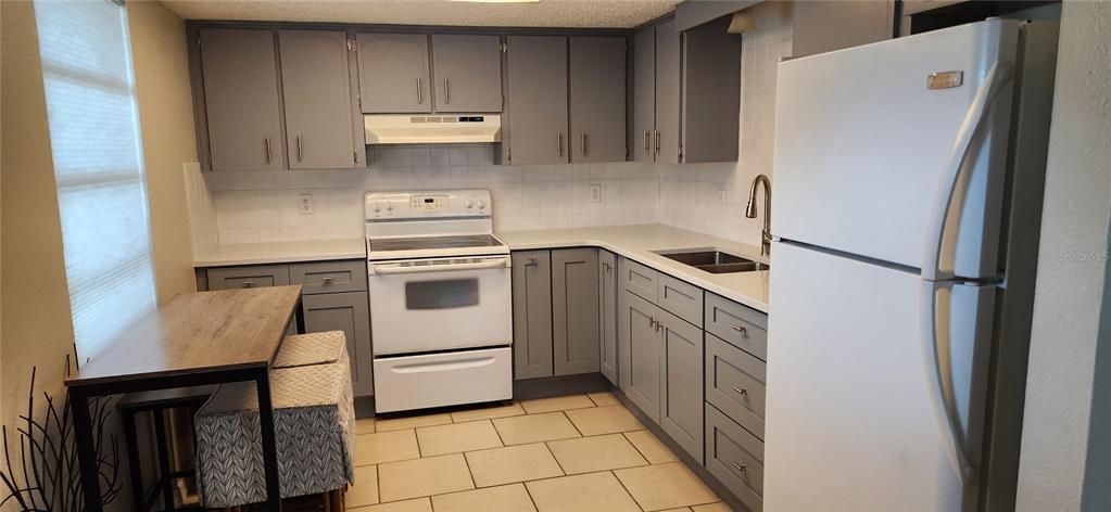 A kitchen features gray cabinets, white appliances, a tiled backsplash, and a small dining table — 5004 AVERY ROAD, NEW PORT RICHEY, FL