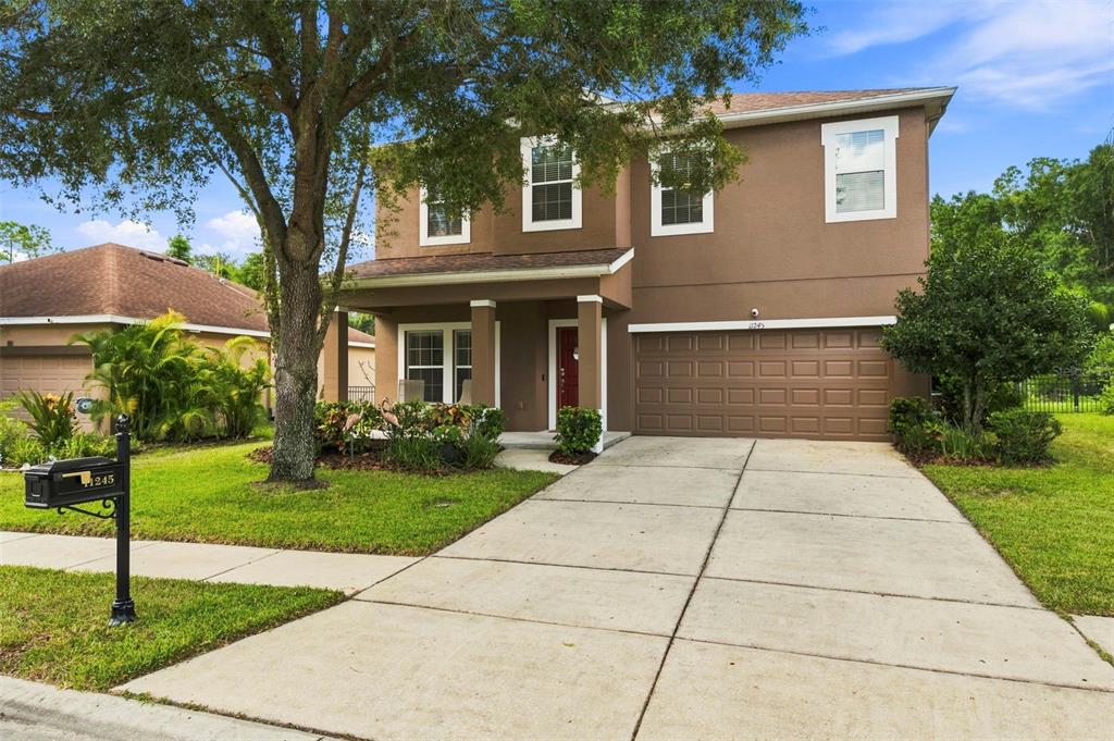 A two-story brown house with a garage, a concrete driveway, and a large front tree — 11245 BELLE HAVEN DRIVE, NEW PORT RICHEY, FL
