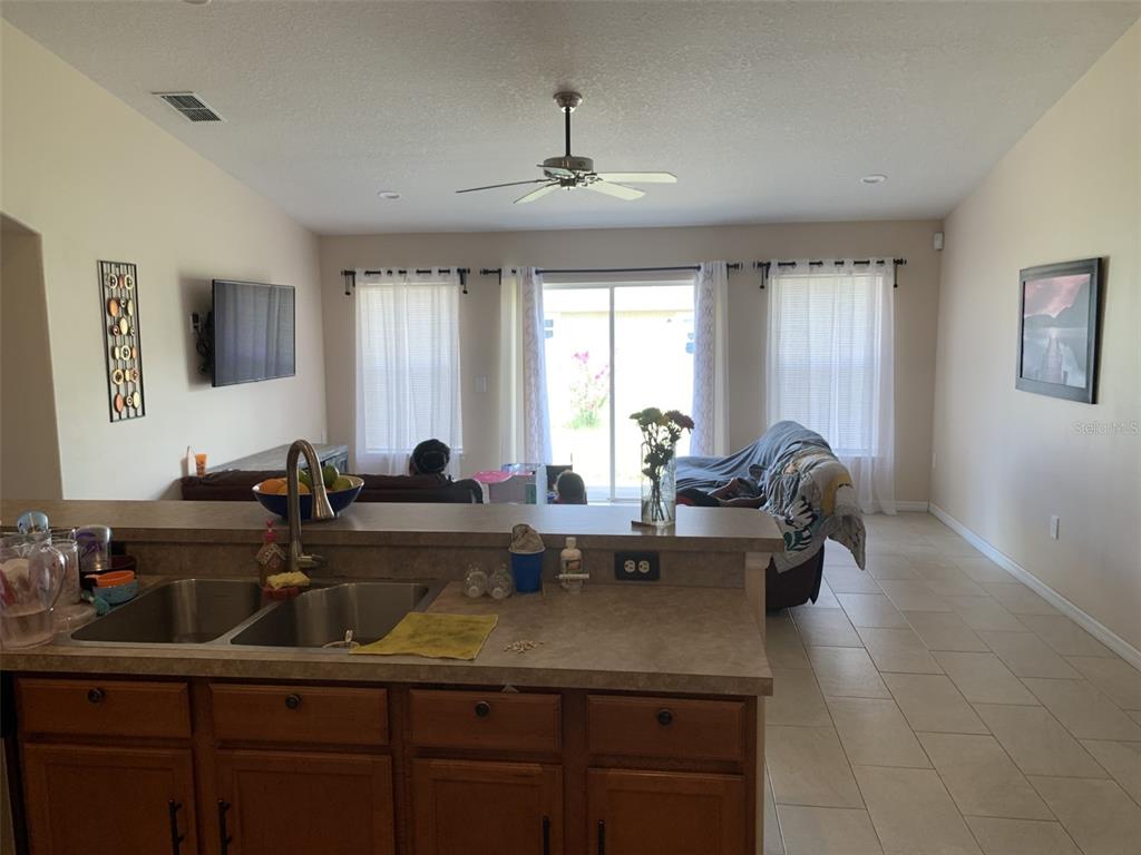 The exterior side of a tan house features a garage, air conditioning unit, and trash bins — 1734 MINNOW COURT, POINCIANA, FL