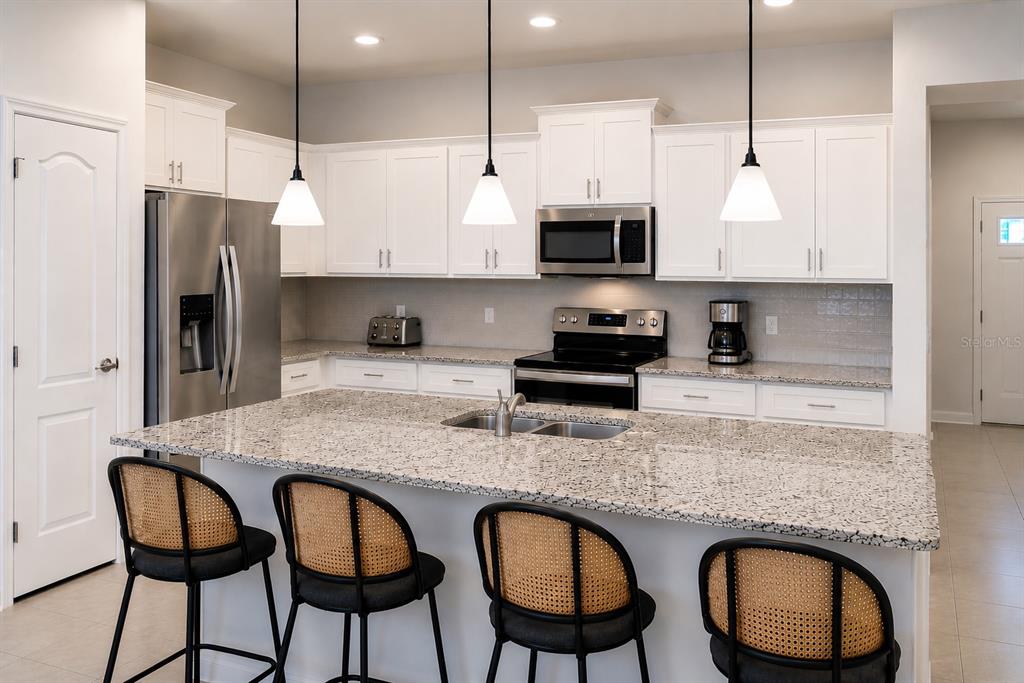 A kitchen features white cabinets, granite countertops, a large island, and four cane-backed bar stools — 2441 DUBAI STREET, KISSIMMEE, FL