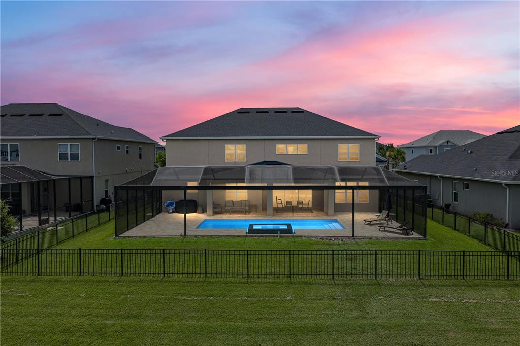 A two-story house features a screened-in pool and patio area in the backyard at sunset — 6978 BRADBURY CIRCLE, WESLEY CHAPEL, FL
