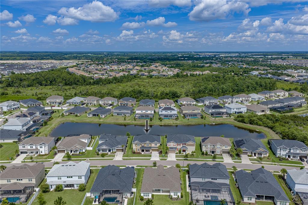 An aerial view shows a suburban neighborhood with houses surrounding a central retention pond — 6978 BRADBURY CIRCLE, WESLEY CHAPEL, FL