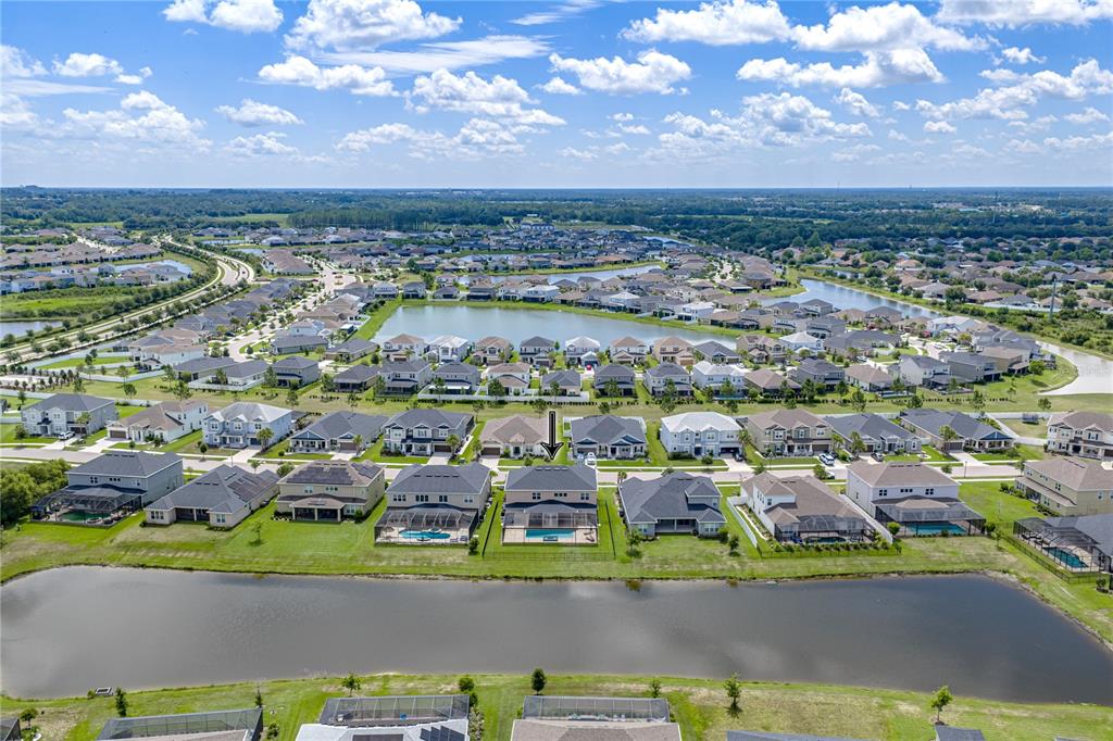 An aerial view shows a suburban neighborhood with houses, swimming pools, and a large pond — 6978 BRADBURY CIRCLE, WESLEY CHAPEL, FL