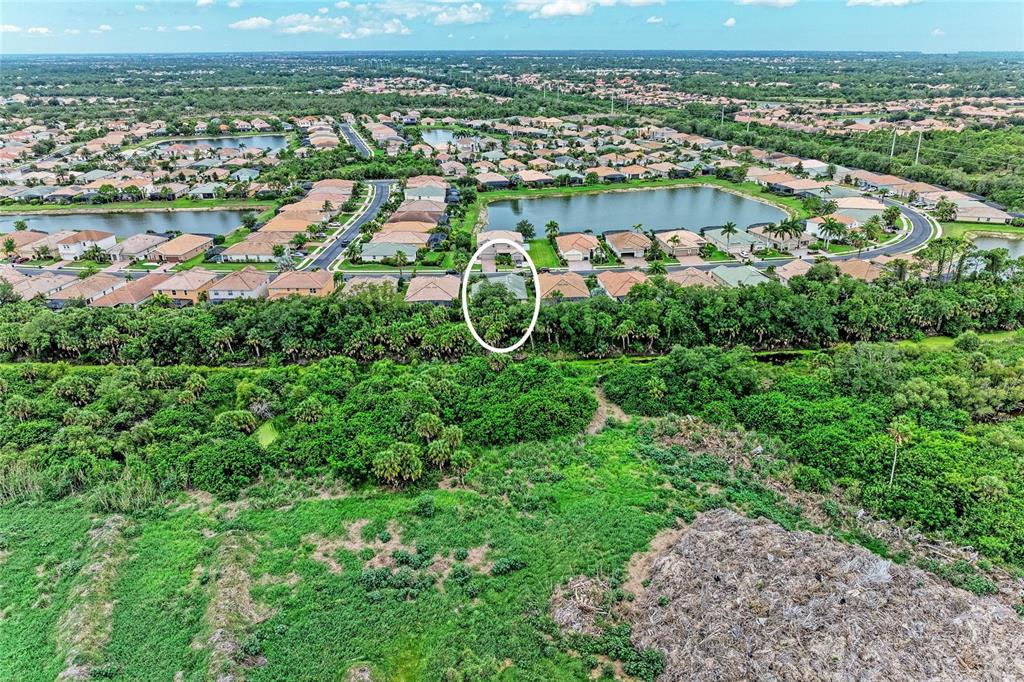 An aerial view shows a residential house circled in a neighborhood bordering a wooded area — 1986 MESIC HAMMOCK WAY, VENICE, FL