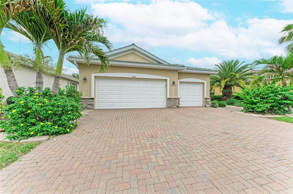 A tan house with a three-car garage and a paved driveway surrounded by palm trees — 1986 MESIC HAMMOCK WAY, VENICE, FL