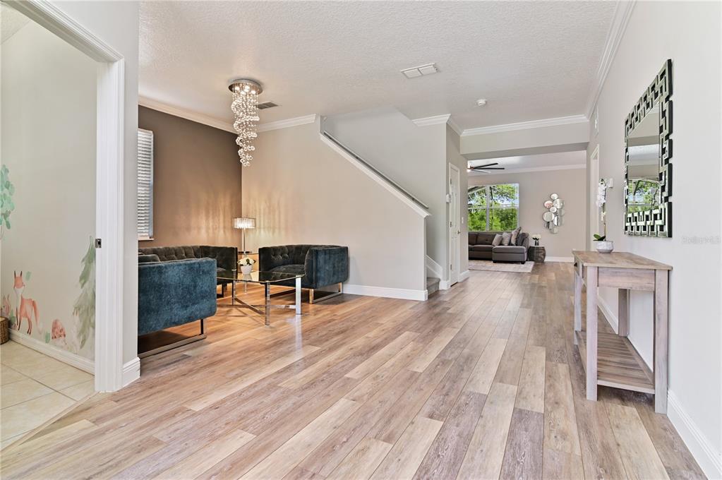 A living area with wood-look flooring, a crystal chandelier, and a staircase leads to another room — 701 KETTERING ROAD, DAVENPORT, FL