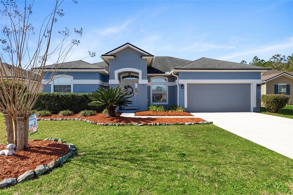 A single-story blue house with a two-car garage, arched entryway, and landscaped front yard — 45095 DUTTON WAY, CALLAHAN, FL