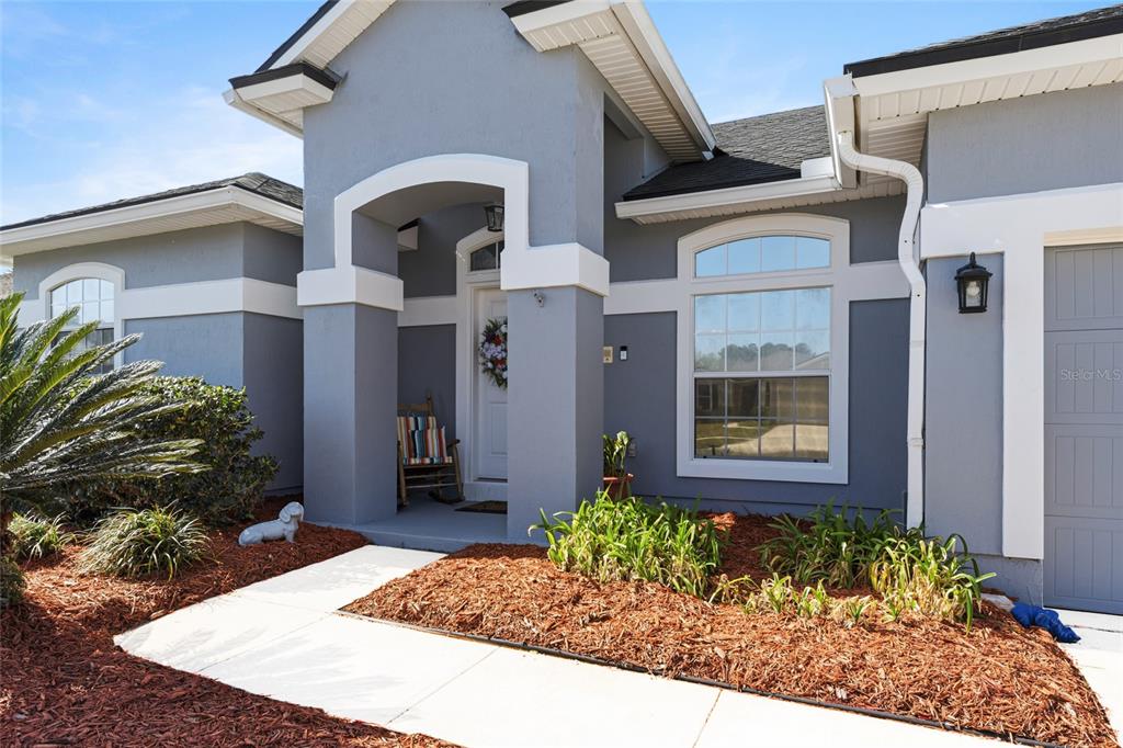 The exterior of a grey house features a covered entryway, a rocking chair, and landscaping — 45095 DUTTON WAY, CALLAHAN, FL