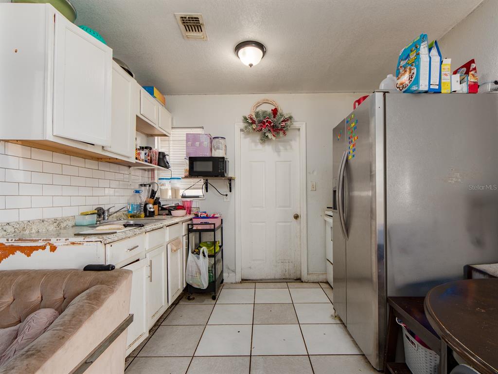 A kitchen features white cabinets, a stainless steel refrigerator, tile flooring, and a white door — 2532 W WALNUT STREET, TAMPA, FL