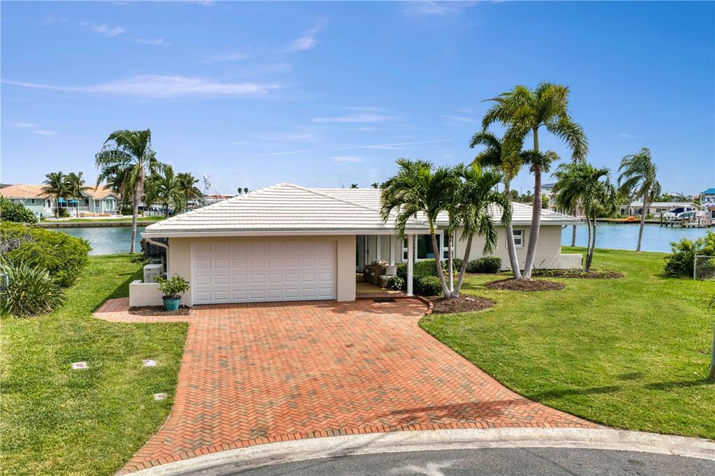 A single-story house with a white garage and brick driveway sits along a canal — 11625 6TH STREET E, TREASURE ISLAND, FL