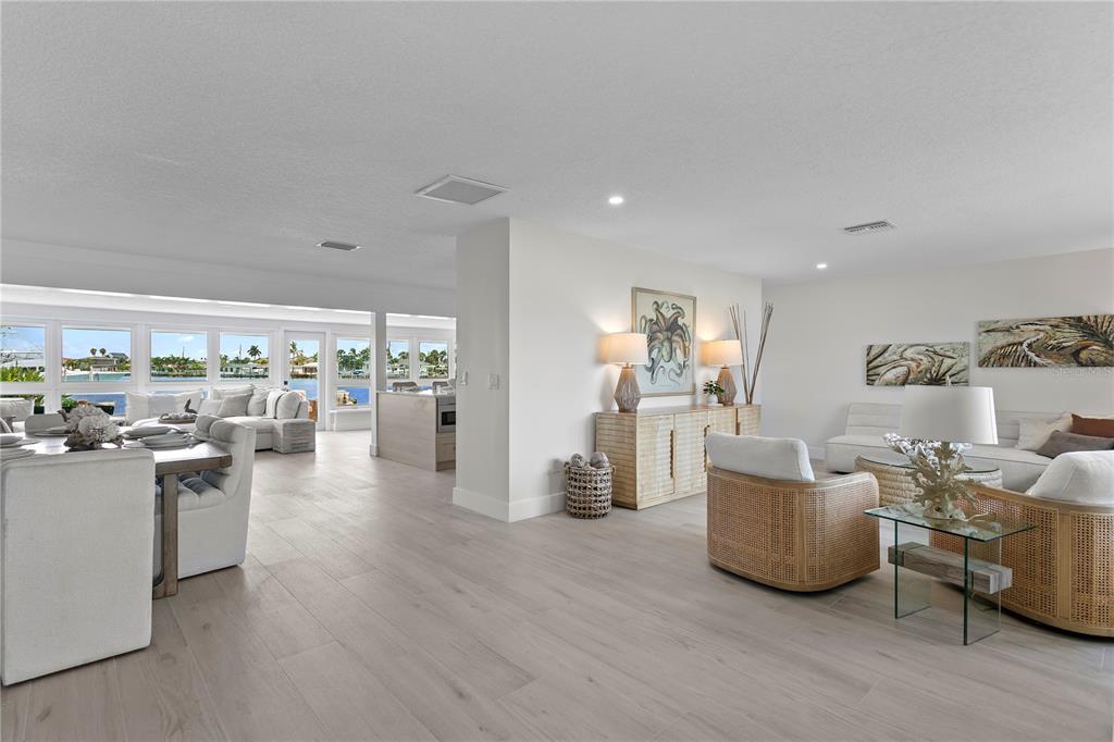 A bright, open-concept living and dining area features light wood flooring and waterfront views — 11625 6TH STREET E, TREASURE ISLAND, FL
