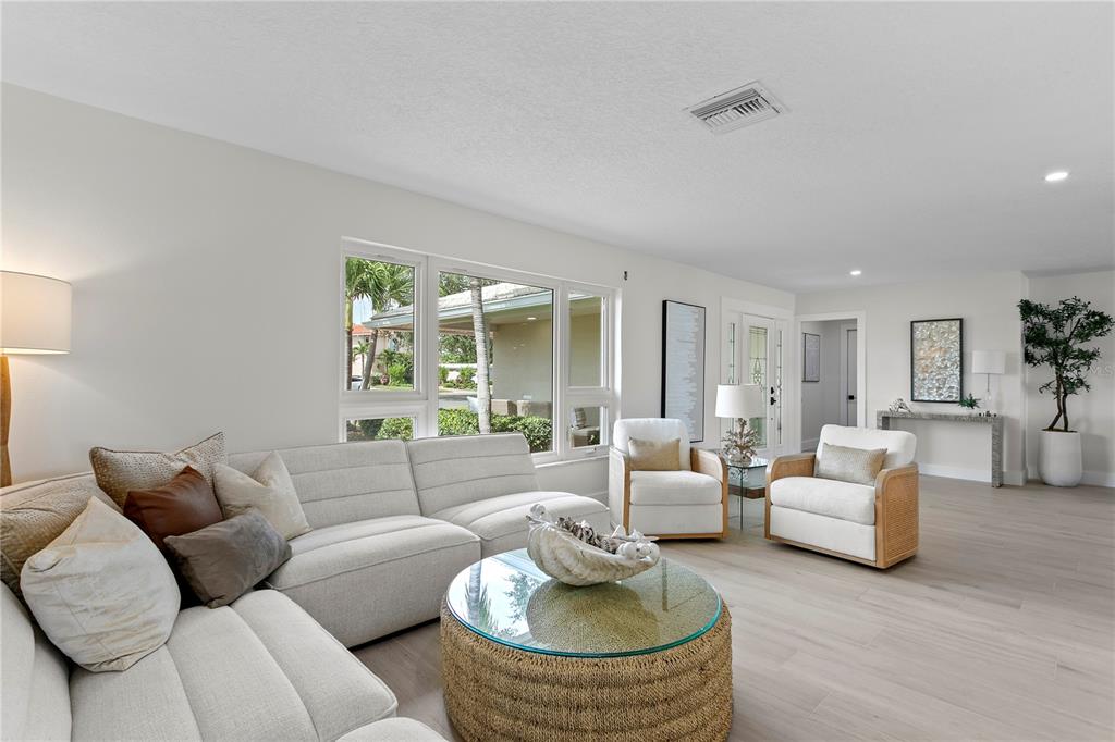 A bright living room features a light-colored sectional, two armchairs, and a round coffee table — 11625 6TH STREET E, TREASURE ISLAND, FL