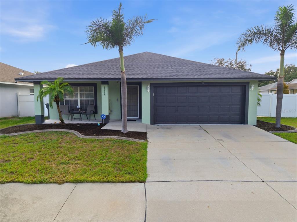 A single-story house with a light green exterior, dark garage door, and two palm trees — 15544 FLORIDA BREEZE LOOP, WIMAUMA, FL