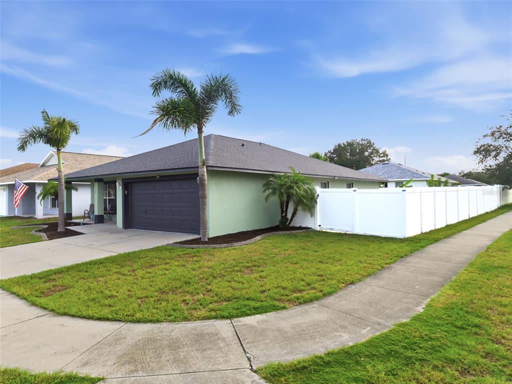 A single-story house with a green exterior, dark garage door, and white vinyl privacy fence — 15544 FLORIDA BREEZE LOOP, WIMAUMA, FL
