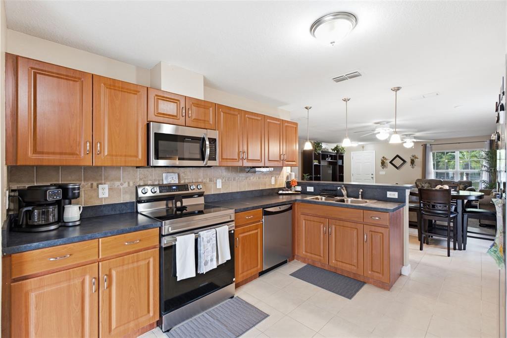 A kitchen with wood cabinets, stainless steel appliances, and dark countertops opens to a dining area — 15544 FLORIDA BREEZE LOOP, WIMAUMA, FL