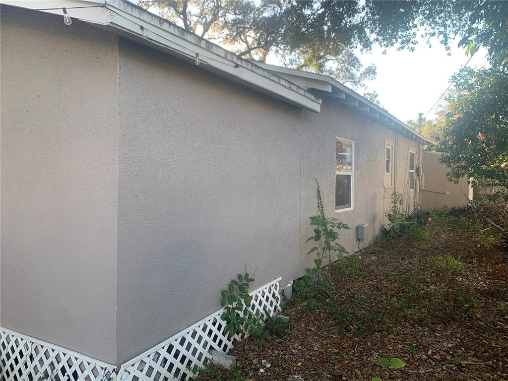 The exterior side of a house features stucco walls, a lattice skirt, and several windows — 1880 SYLVAN DRIVE, CLEARWATER, FL