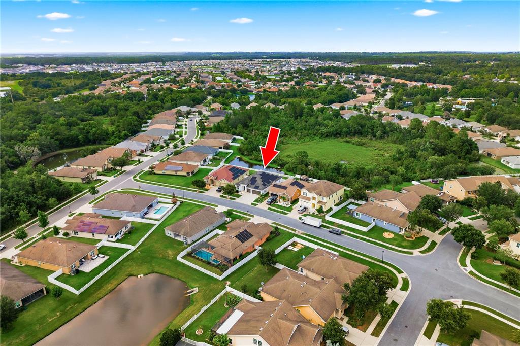An aerial view of a suburban neighborhood featuring a house marked with a red arrow — 6410 FALLING OAK TRAIL, WESLEY CHAPEL, FL