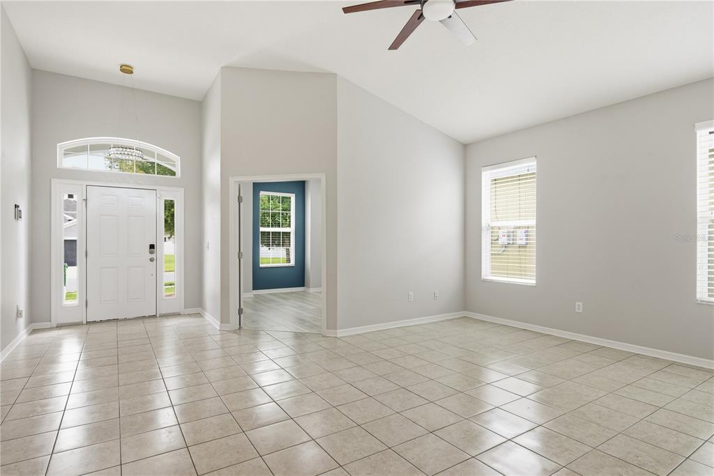 A bright, tiled living room features a vaulted ceiling, a ceiling fan, and an entryway — 6410 FALLING OAK TRAIL, WESLEY CHAPEL, FL