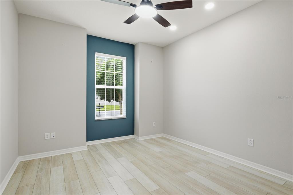 An empty bedroom features light wood-look tile flooring, a blue accent wall, and a ceiling fan — 6410 FALLING OAK TRAIL, WESLEY CHAPEL, FL