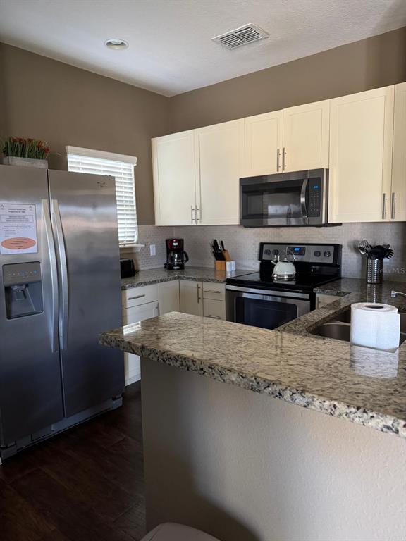 A kitchen features stainless steel appliances, off-white cabinets, and granite countertops — 8981 SHINE DRIVE, KISSIMMEE, FL