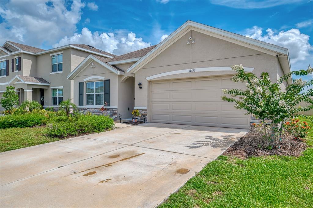 A beige single-story house with a two-car garage, stone accents, and a concrete driveway — 17733 CANOPY PLACE, BRADENTON, FL