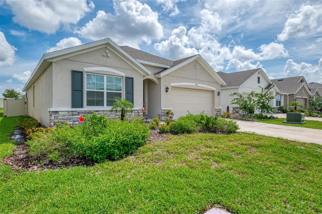 A single-story suburban house with a tan stucco exterior, stone accents, and a two-car garage — 17733 CANOPY PLACE, BRADENTON, FL