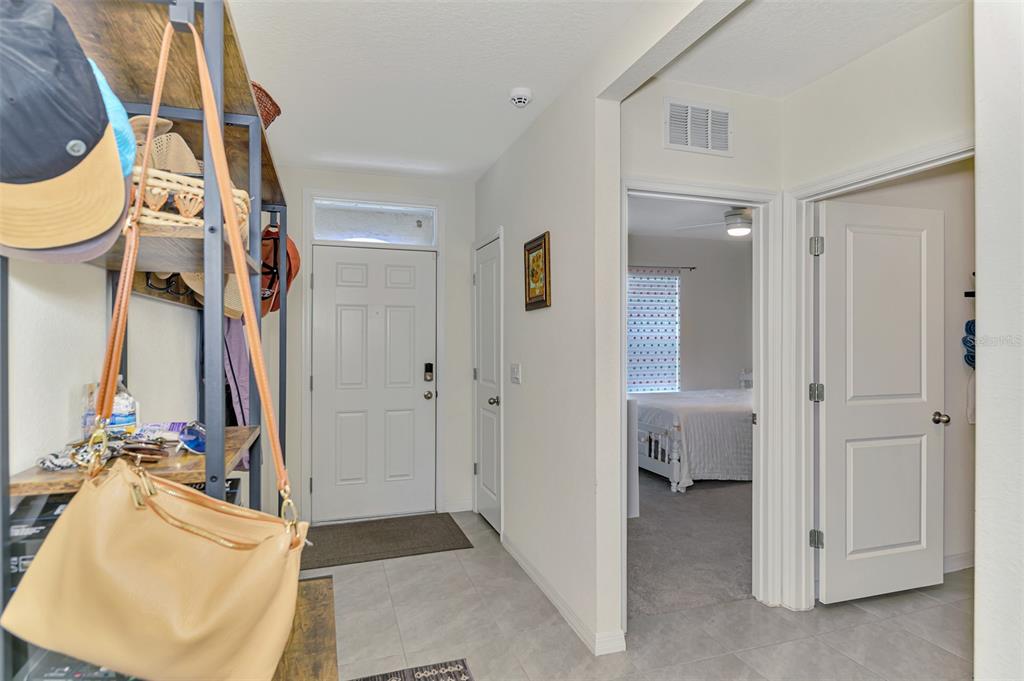 An entryway with a storage rack, a front door, and a view into a bedroom — 17733 CANOPY PLACE, BRADENTON, FL