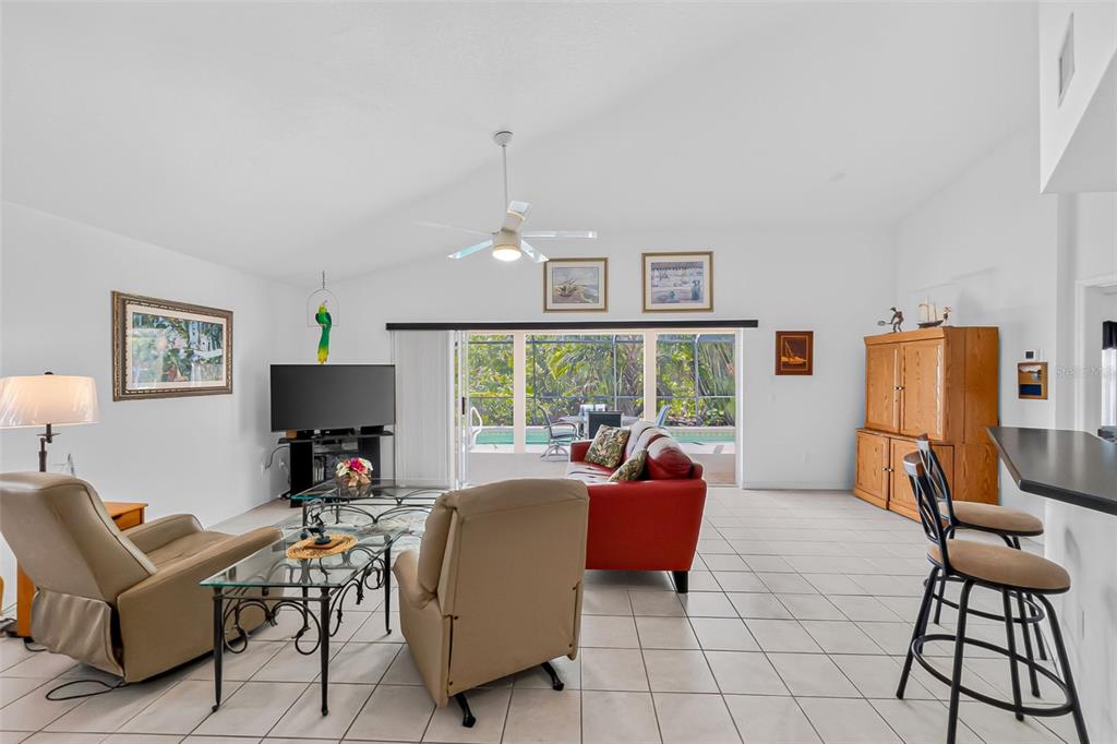 A living room with tile floors, a red sofa, two recliners, and a sliding glass door — 3901 CAPE COLE BOULEVARD, PUNTA GORDA, FL