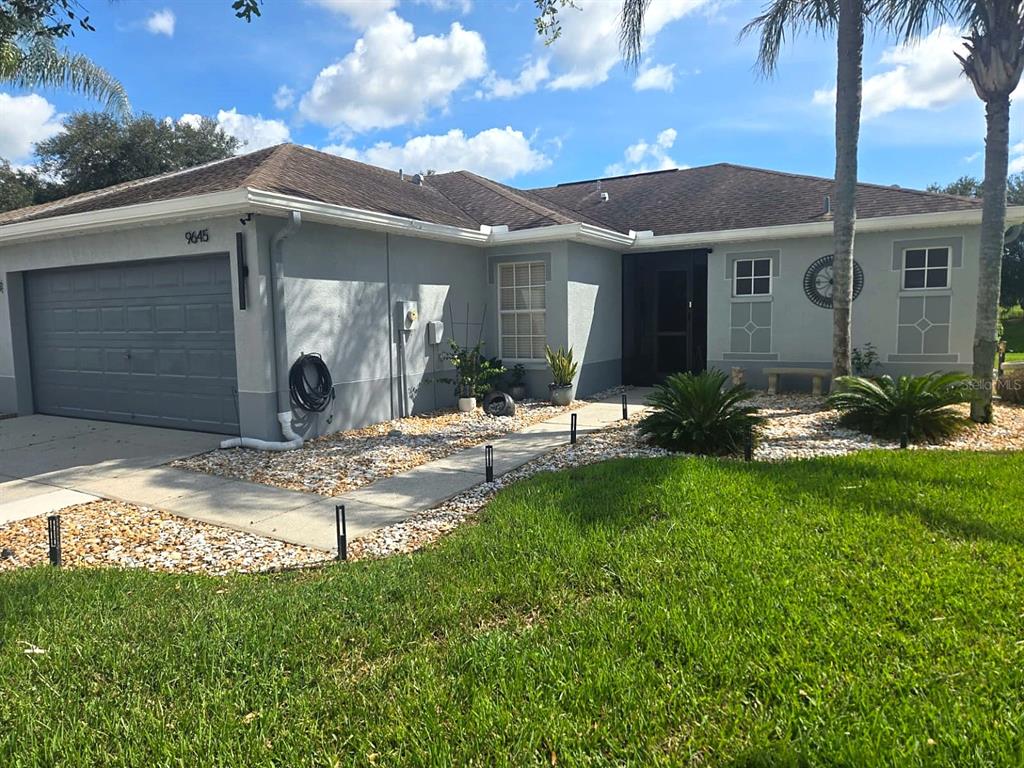 A single-story house with a gray exterior, a two-car garage, and a landscaped front yard — 9645 ROLLING CIRCLE, SAN ANTONIO, FL