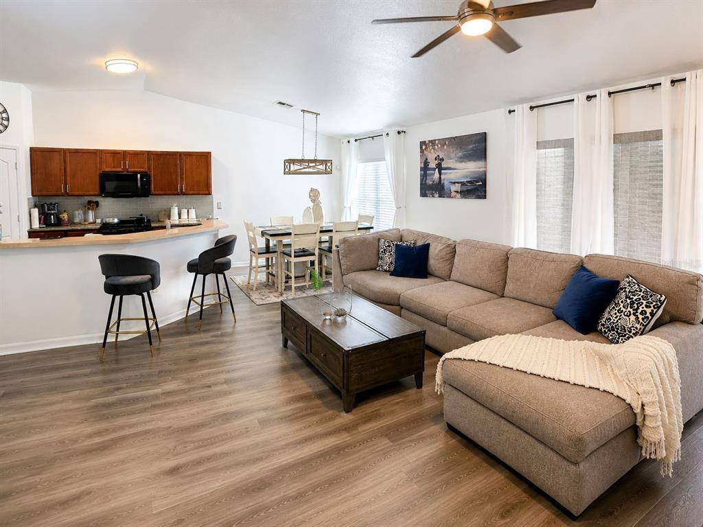 An open-concept living and dining area features wood-look flooring, a sectional sofa, and kitchen bar seating — 9645 ROLLING CIRCLE, SAN ANTONIO, FL