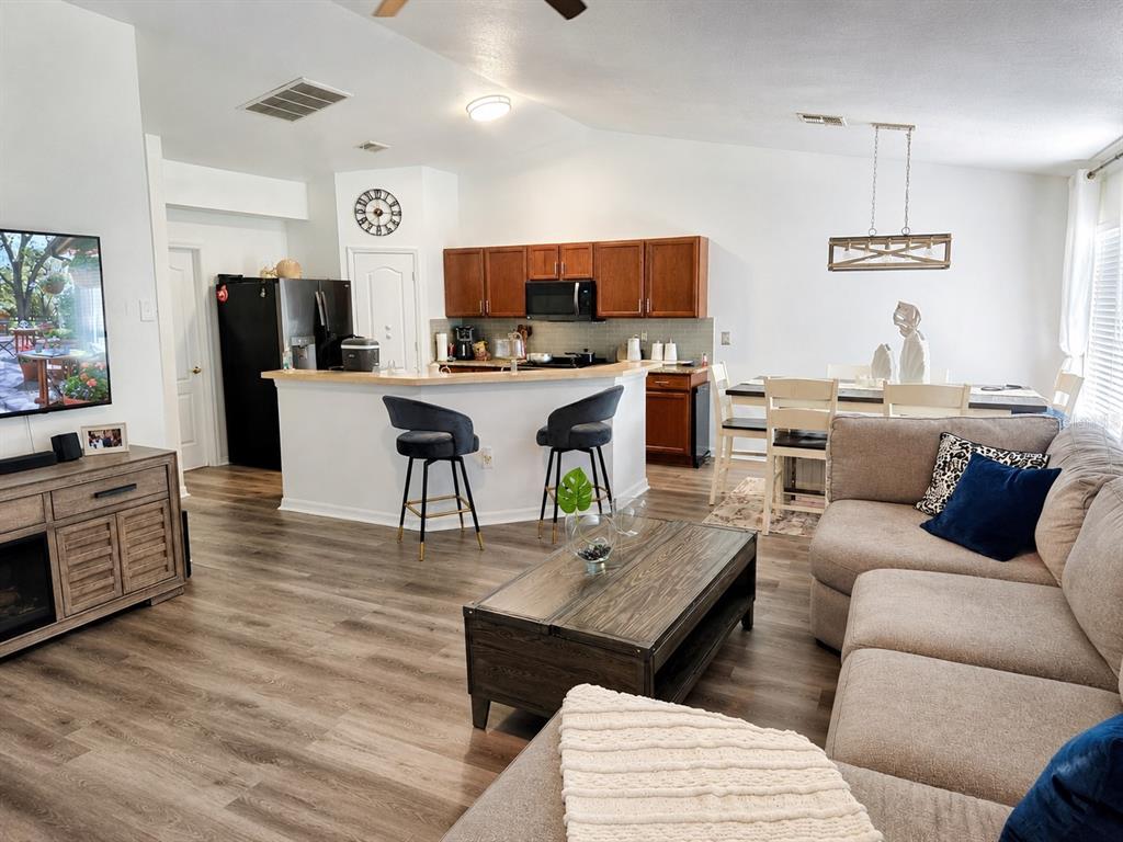 An open-concept living room and kitchen featuring wood-look flooring, a breakfast bar, and dining area — 9645 ROLLING CIRCLE, SAN ANTONIO, FL