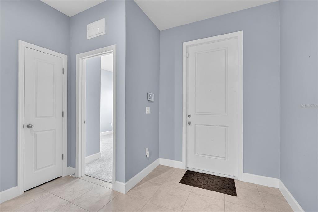 An entryway features light blue walls, tile flooring, a white front door, and two doorways — 9810 EVENTIDE TRAIL, PARRISH, FL