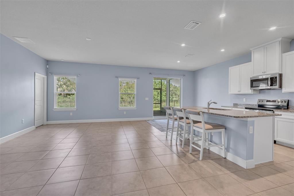 A kitchen with a granite island and bar stools opens into a spacious, light-blue living area — 9810 EVENTIDE TRAIL, PARRISH, FL