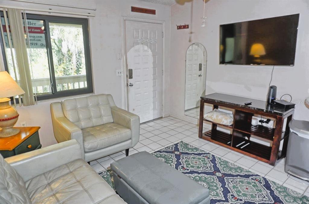A living room features white tile floors, a gray leather armchair, and a wall-mounted television — 20893 HAULOVER COVE UNIT E8, LUTZ, FL