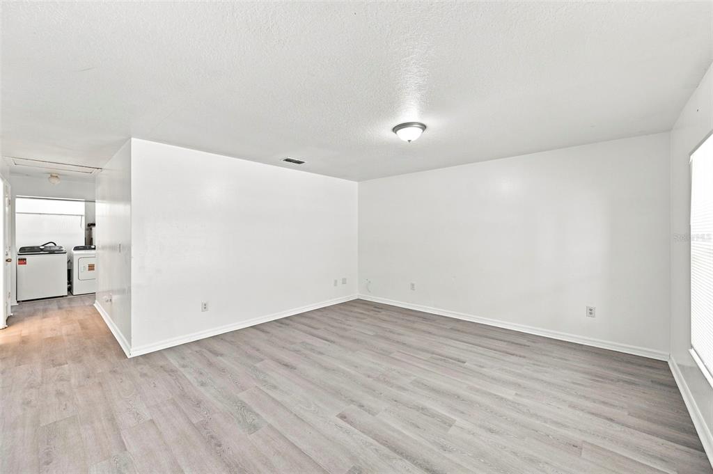 An empty room with white walls and light wood-look flooring leads to a laundry area — 980 13TH AVENUE S, ST PETERSBURG, FL