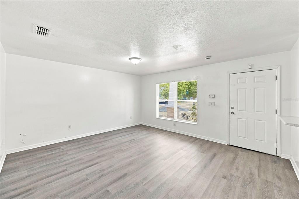 An empty living room with white walls, light gray wood-look flooring, and a white door — 980 13TH AVENUE S, ST PETERSBURG, FL