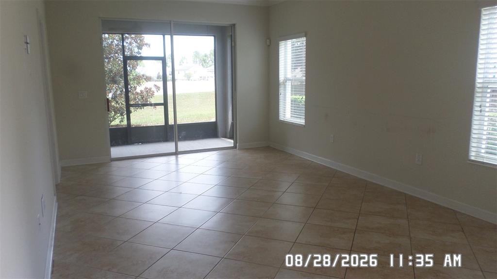 An empty room with beige tile flooring, two windows, and a sliding glass door — 3547 FAIRWATERS COURT UNIT F, CLERMONT, FL