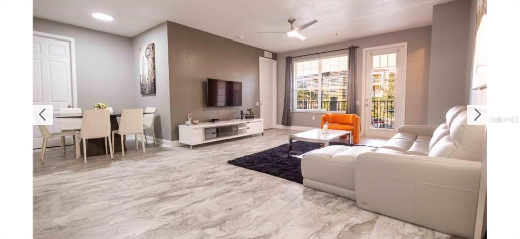 A modern living and dining area features light wood-look flooring, gray walls, and white furniture — 5024 SHOREWAY LOOP UNIT 20106, ORLANDO, FL