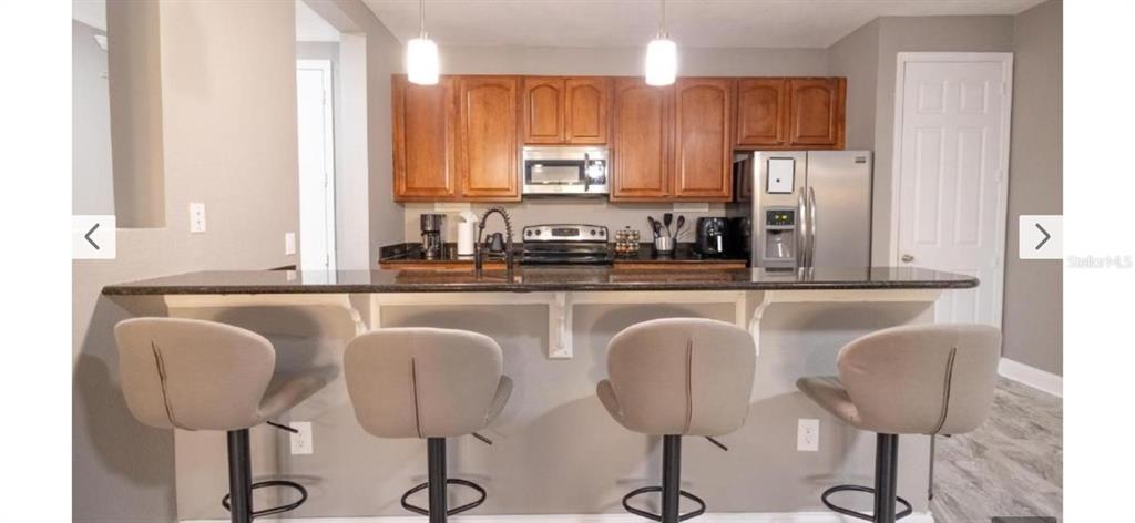 A kitchen features wood cabinets, stainless steel appliances, a dark countertop, and four bar stools — 5024 SHOREWAY LOOP UNIT 20106, ORLANDO, FL