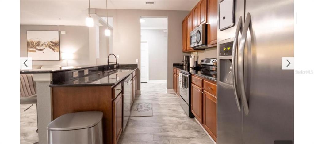A kitchen features wood cabinets, stainless steel appliances, and a dark countertop breakfast bar — 5024 SHOREWAY LOOP UNIT 20106, ORLANDO, FL