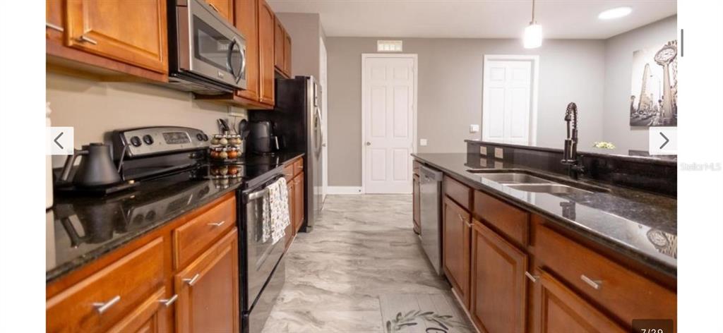A kitchen features wood cabinets, black countertops, stainless steel appliances, and light-colored flooring — 5024 SHOREWAY LOOP UNIT 20106, ORLANDO, FL