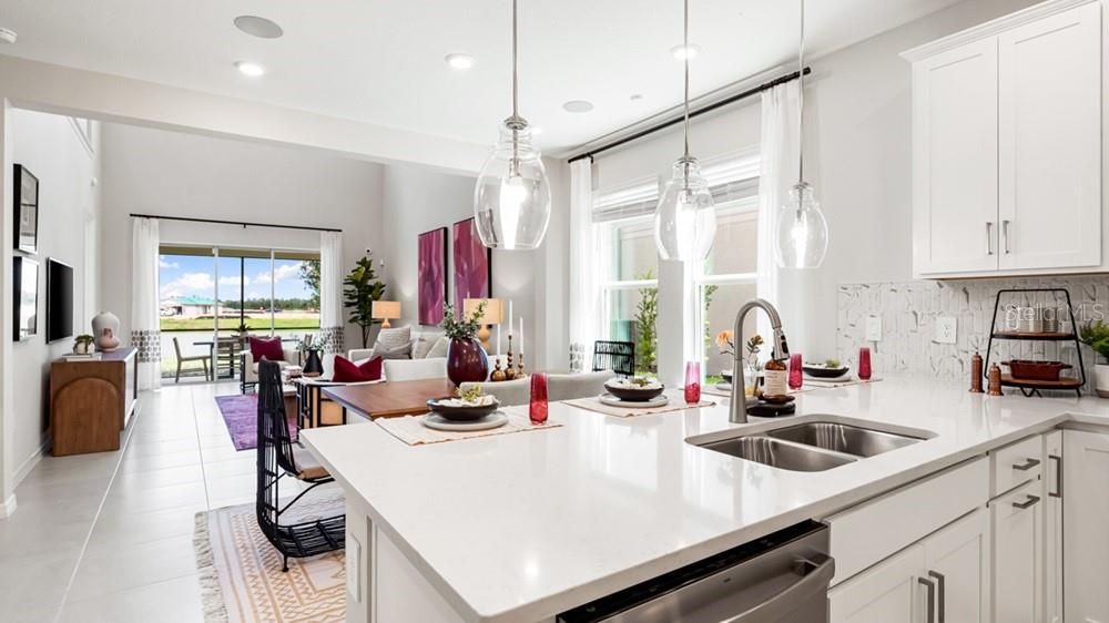 A bright, open-concept kitchen with white cabinetry and quartz countertops overlooks a living area — 11400 STRONG STEM ROW, SAN ANTONIO, FL