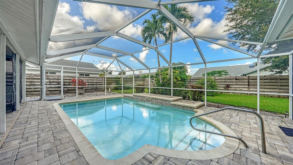 A screened-in swimming pool with a stone patio and a wooden privacy fence in the backyard — 4494 DIAMOND CIRCLE E, SARASOTA, FL