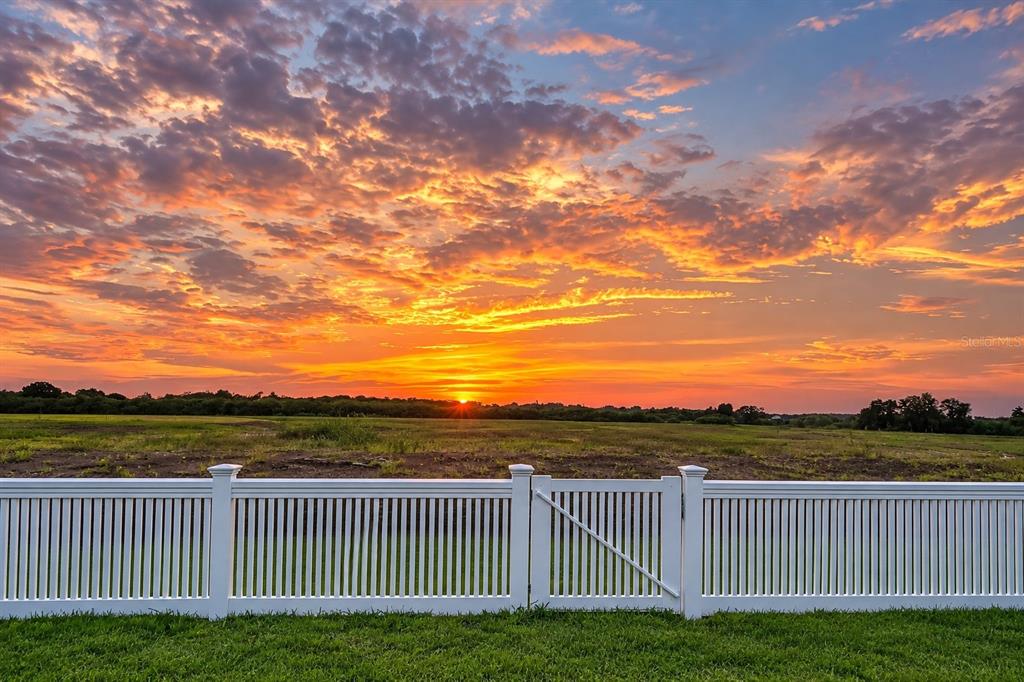 A white vinyl fence stands in front of a grassy field under a vibrant sunset sky — 3519 NIGHT STAR TERRACE, PARRISH, FL