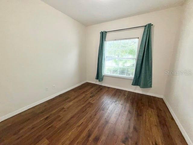 An empty room features light-colored walls, wood-look flooring, and a window with teal curtains — 4301 HEIRLOOM ROSE PLACE, OVIEDO, FL