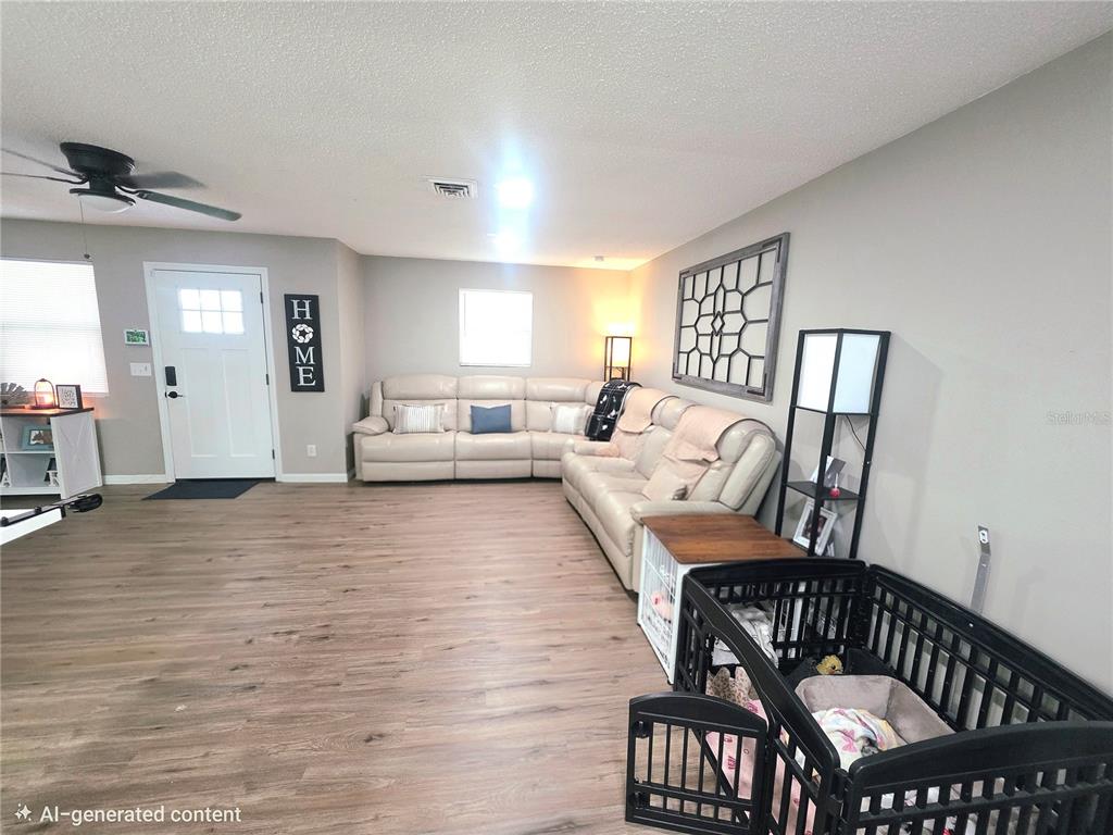 This living room features light wood-look flooring, a large sectional sofa, and a pet crate — 1380 EAGLE AVENUE E, EAGLE LAKE, FL