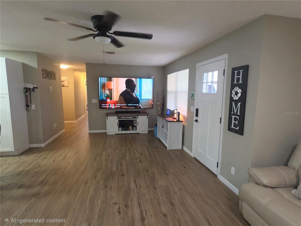 This living room features wood-look flooring, a ceiling fan, a wall-mounted television, and a front door — 1380 EAGLE AVENUE E, EAGLE LAKE, FL
