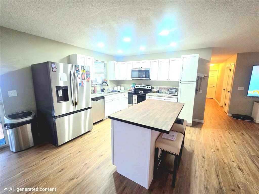 A kitchen features white cabinetry, stainless steel appliances, a wood-topped island, and light wood flooring — 1380 EAGLE AVENUE E, EAGLE LAKE, FL